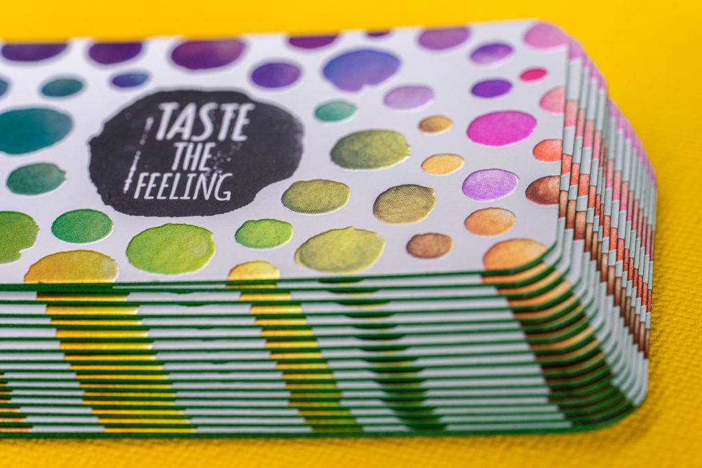 28 pt cold foil business cards with colorful polka dots and “Taste the Feeling” in a purple circle