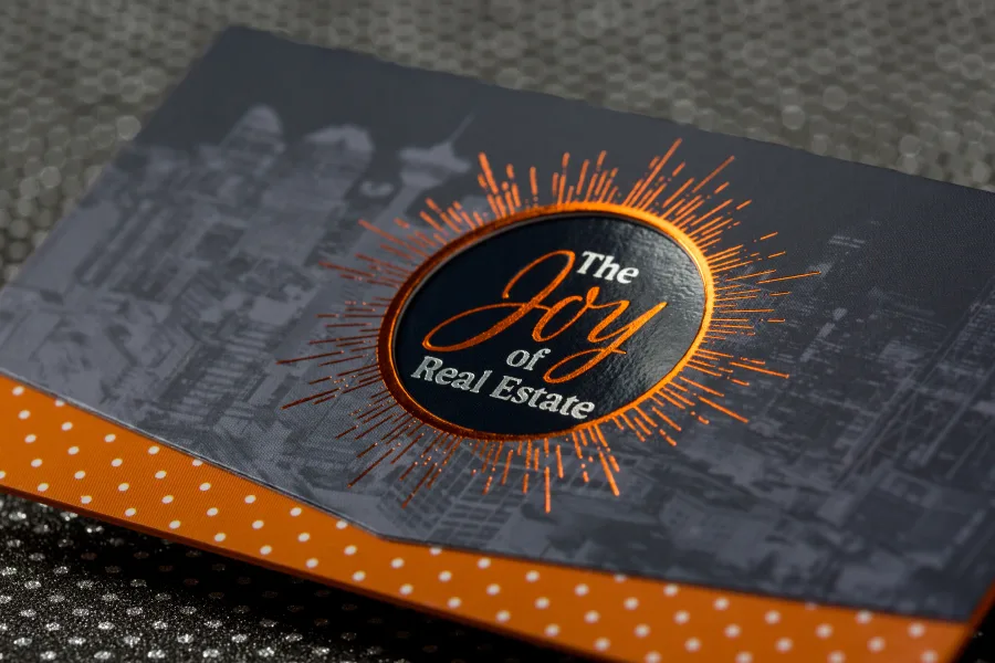 Suede business card with a colored foil sunburst design and orange colored edges, for a real estate brand