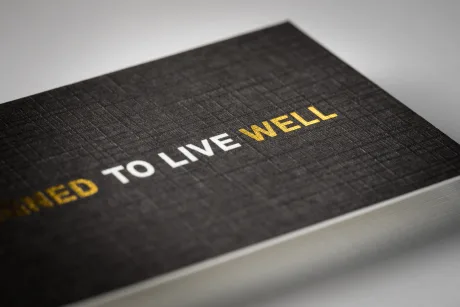 Extreme close-up of dark linen card stock showing the woven paper texture with white and gold foil lettering
