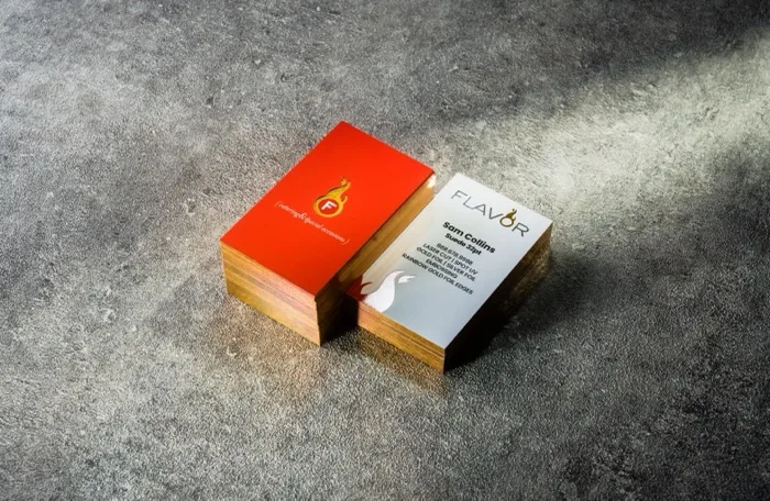 A glossy red Spot UV "Flavor Catering" card next to a cream Suede 32pt card with a foiled copper edge.