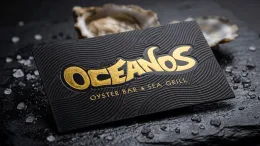 After: a black business card with raised gold foil lettering and a fine debossed wave texture.