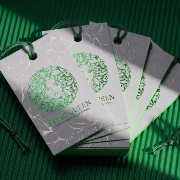 A fanned stack of gray hang tags with green foil lettering, showing the layered edge thickness.
