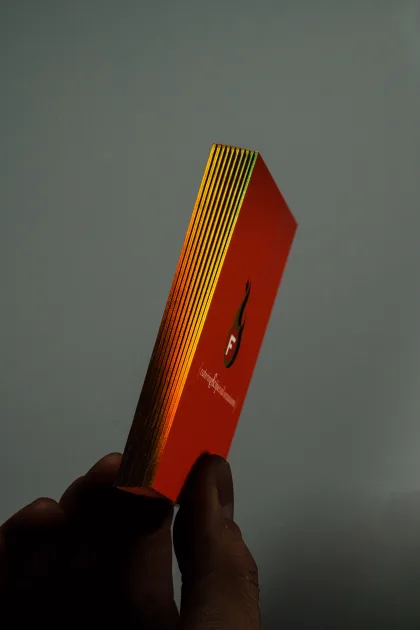 A stack of thick red business cards held in a hand, showing gold foiled edges and a flame emblem on the face.