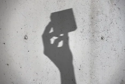The shadow of a hand holding a small product package, cast against a concrete wall.