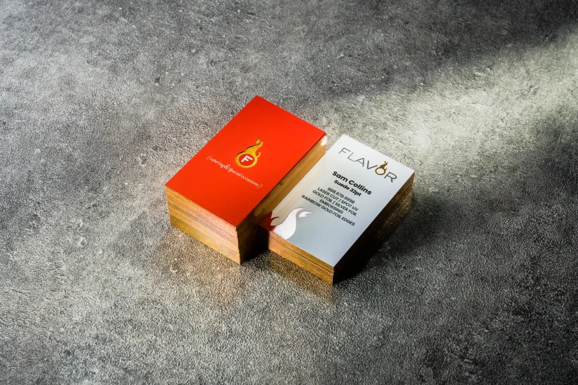 A stack of red "Flavor" catering business cards with rainbow gold foiled edges.