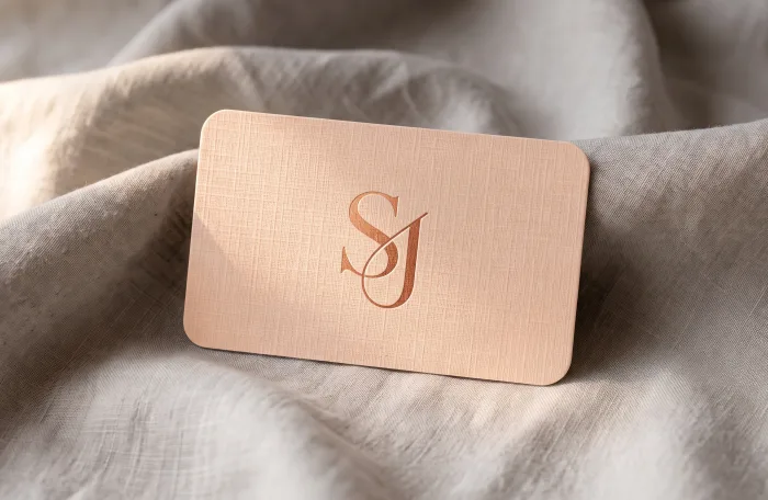 A blush Linen business card with a debossed rose-gold monogram, resting on linen fabric