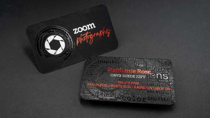 Two onyx black suede business cards — one for Zoom Photography with a white and red foil camera-shutter logo, and a spec card labeled "Onyx Suede 22pt" listing red foil, white foil, raised UV, and spot UV finishes.