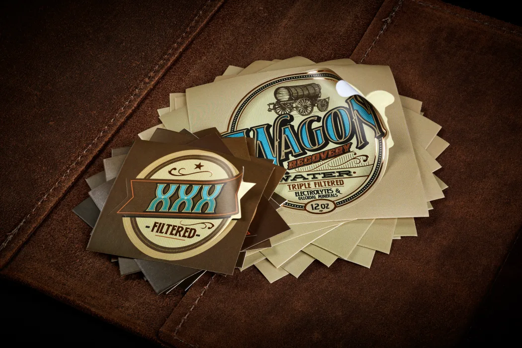 A stack of round die-cut label stickers with a gold foil rim, cut clean to the badge shape, resting on leather.